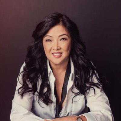 A woman with long black hair sitting in front of a wall.